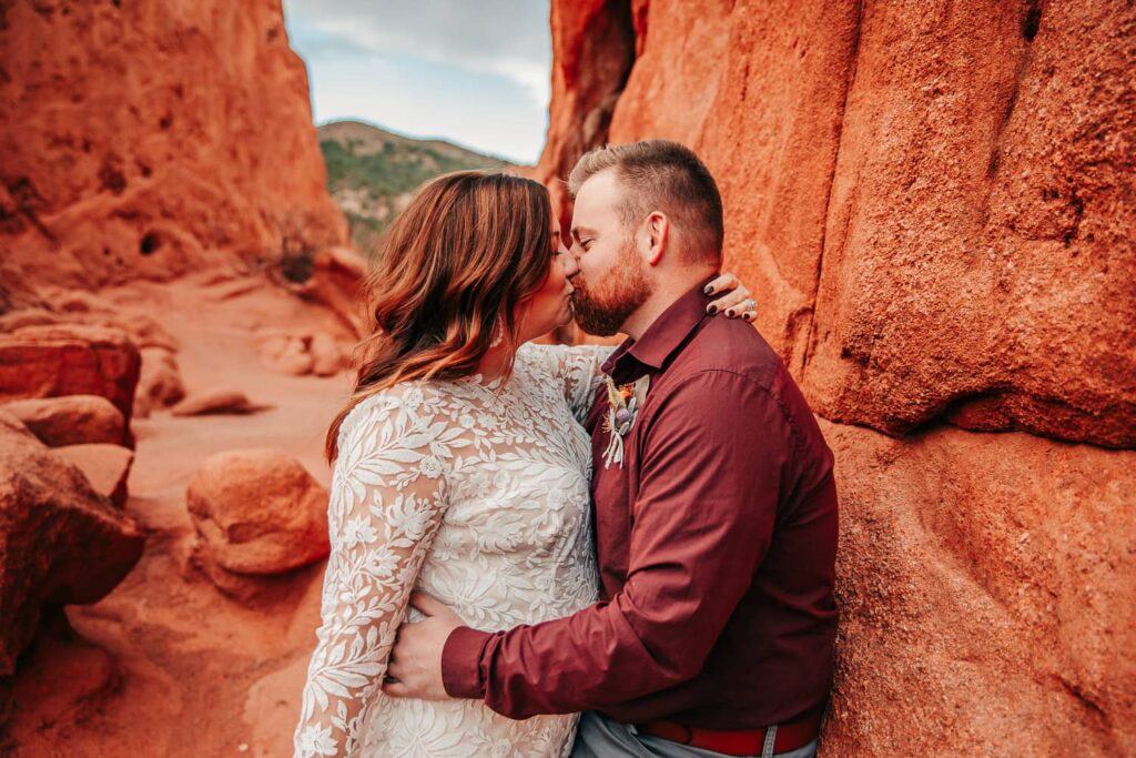 A couple in wedding attire kissing in a red rock canyon.