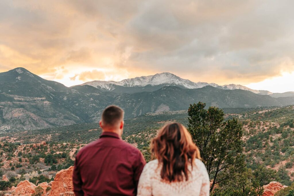 A couple in wedding attire standing and gazing out at Pikes Peak in Garden of the Gods.
