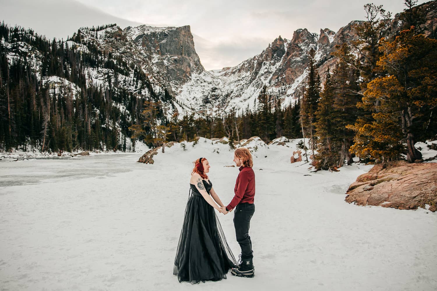 A couple holding hands wearing formal attire on a frozen alpine lake in Rocky Mountain National Park.