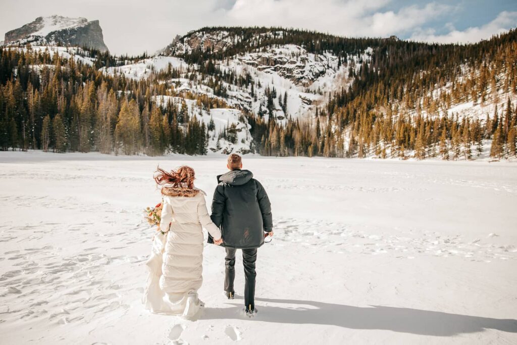 A couple walking away on a frozen mountain lake in Colorado. They are in winter wedding attire.