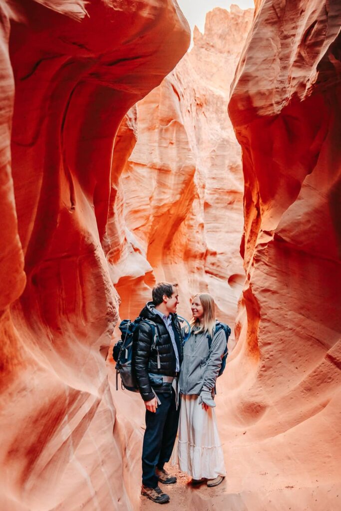A couple in wedding attire standing in a slot canyon looking at each other.
