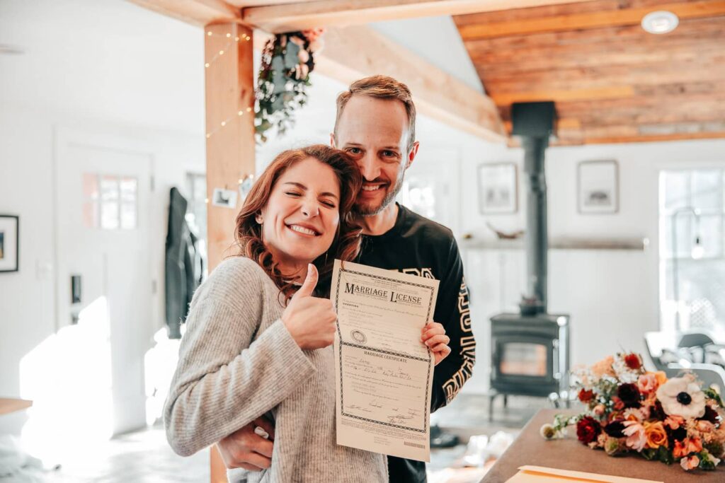 A couple in casual attire on their wedding day holding their Colorado marriage license.