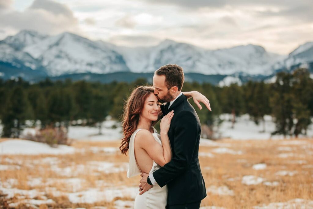 A groom kissing his bride's forehead during their colorado elopement in Rocky Mountain National Park.