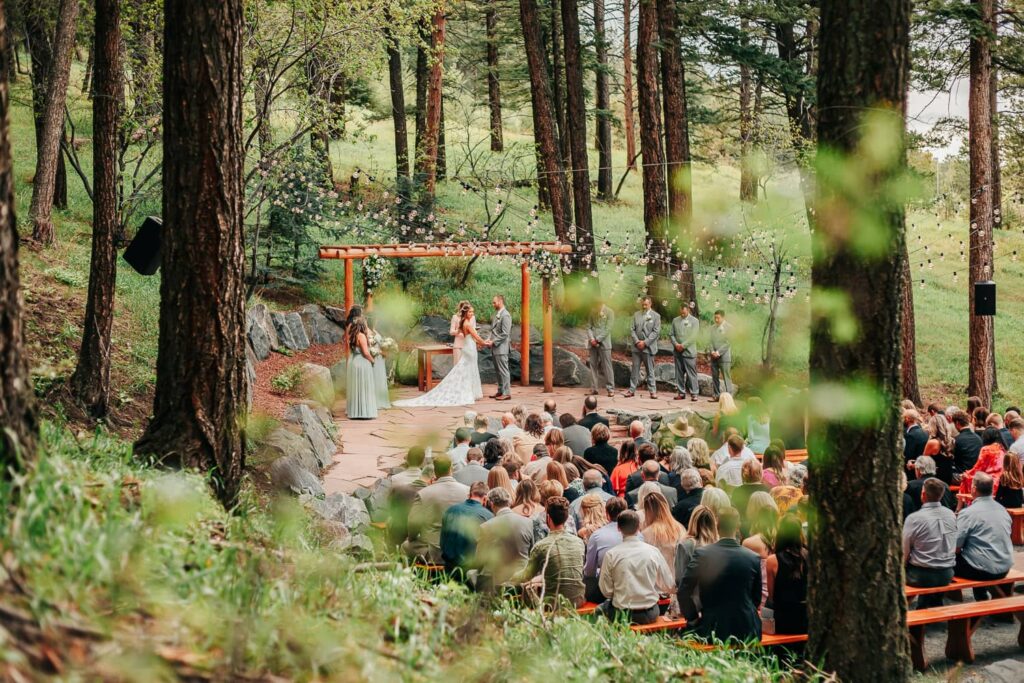 A couple in wedding attire during their colorado wedding ceremony. They are standing at the alter holding hands and the bride is looking out at their guests. The Pines Wedding venue.