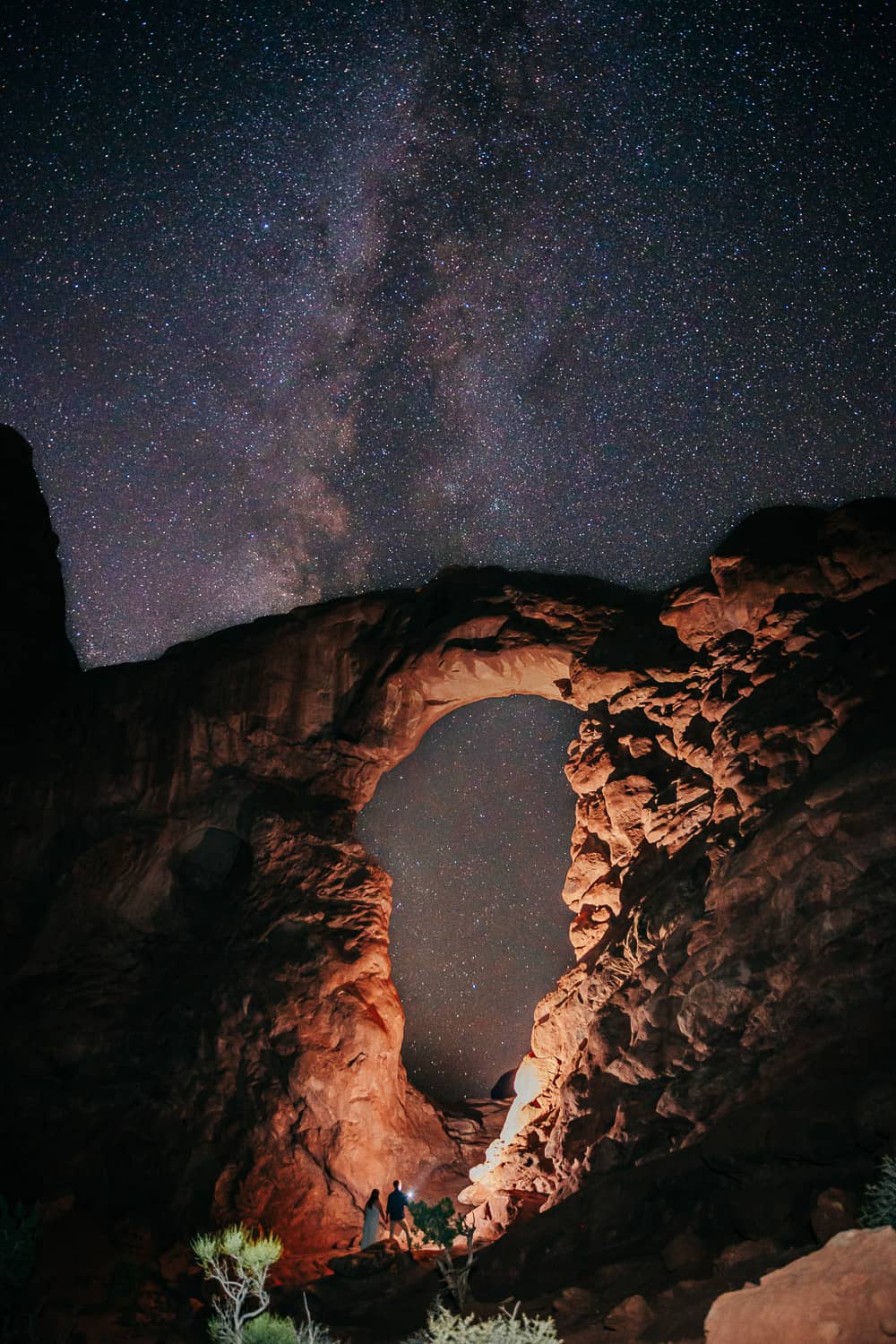 Couple standing at the base of turret arch, it is night time and they are lighting up the arch with a flashlight