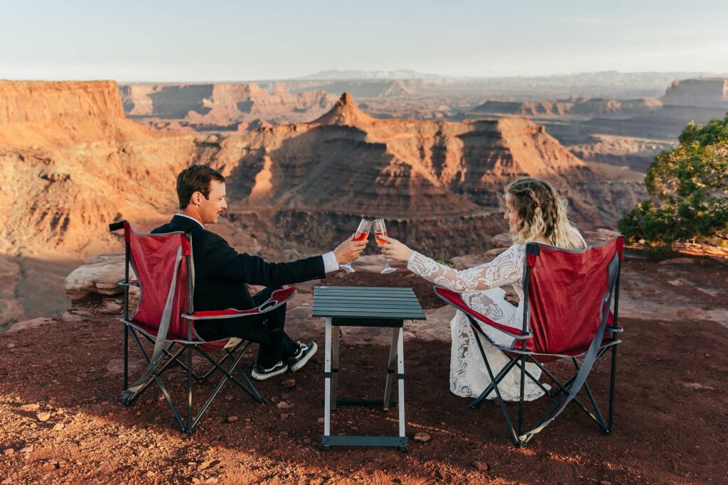A couple clinking glasses while sitting in camping chairs during their utah elopement.