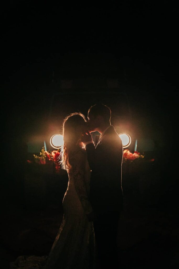 A groom kissing his bride during their Moab elopement. They are standing in front of their jeep's headlights.