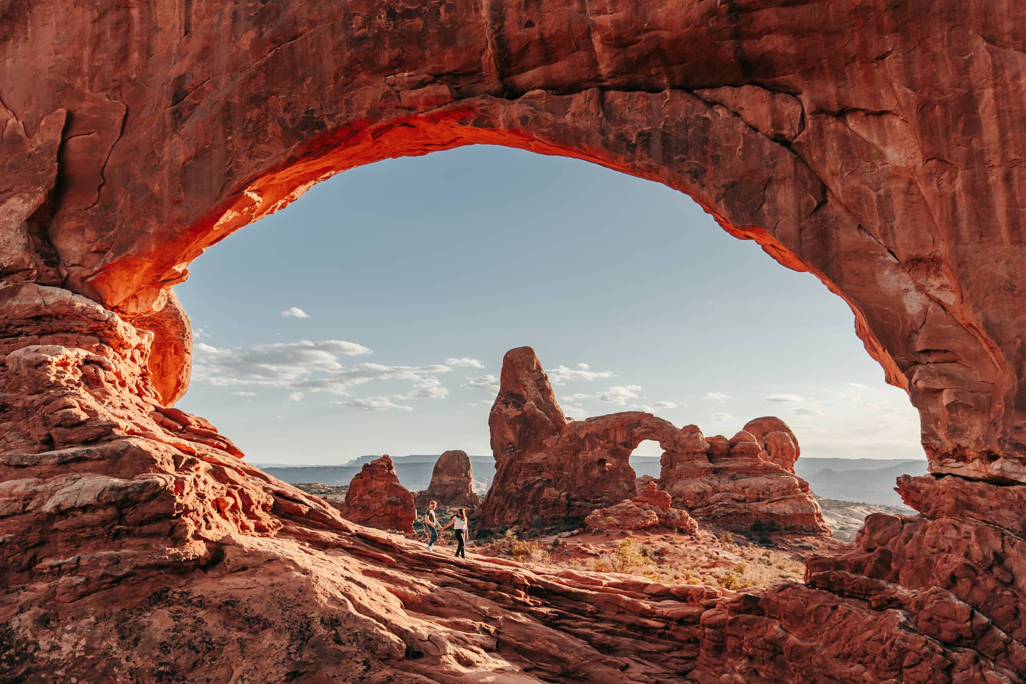 Couple walking under a large arch in arches national park